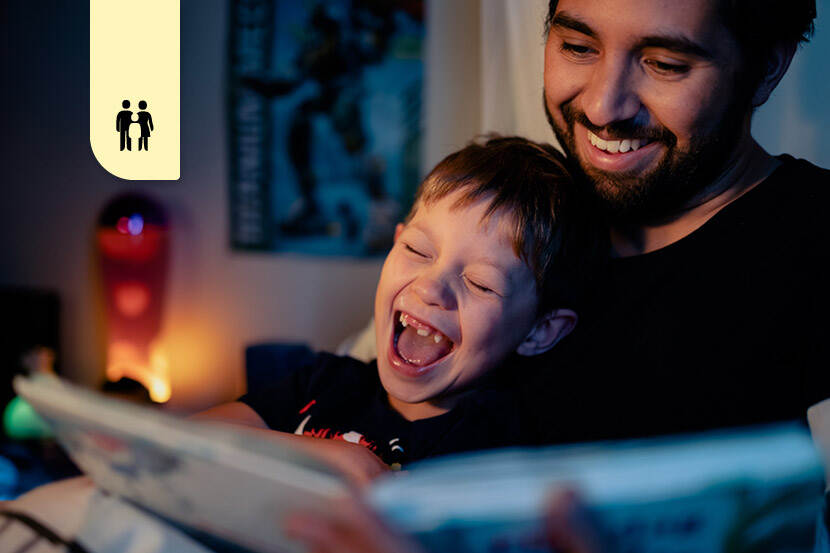 Vader en zoon lezen samen een boek op de bank. De jonge jongen lacht heel hard, terwijl zijn vader voorleest.